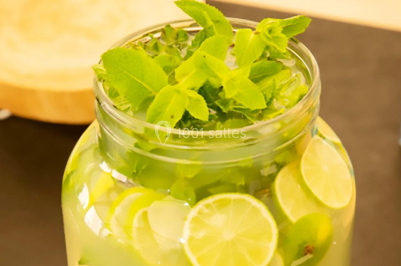 Bocal de limonade maison avec des tranches de citron vert et des feuilles de menthe fraîche.