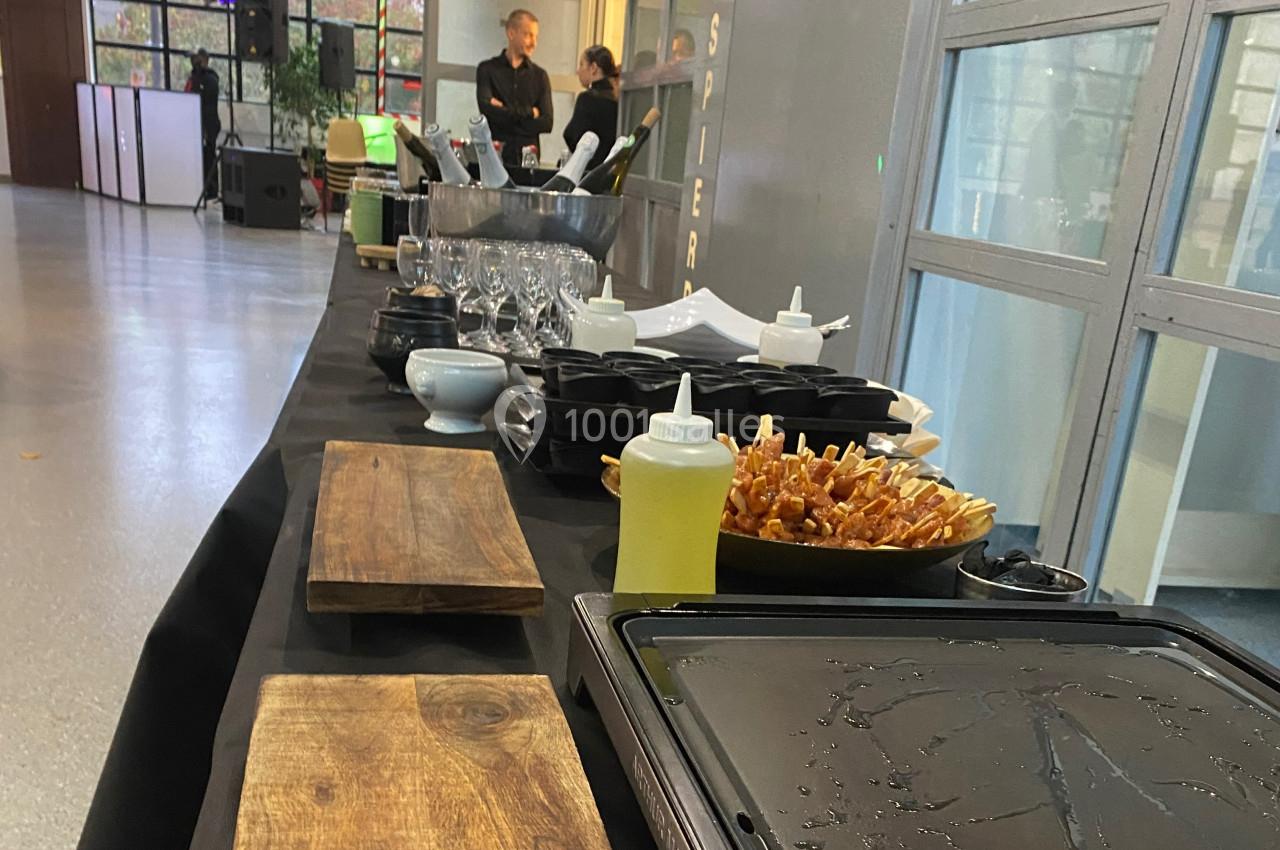 Table de buffet avec planches en bois, verrerie, bouteilles, sauces et amuse-bouches dans une salle lumineuse.