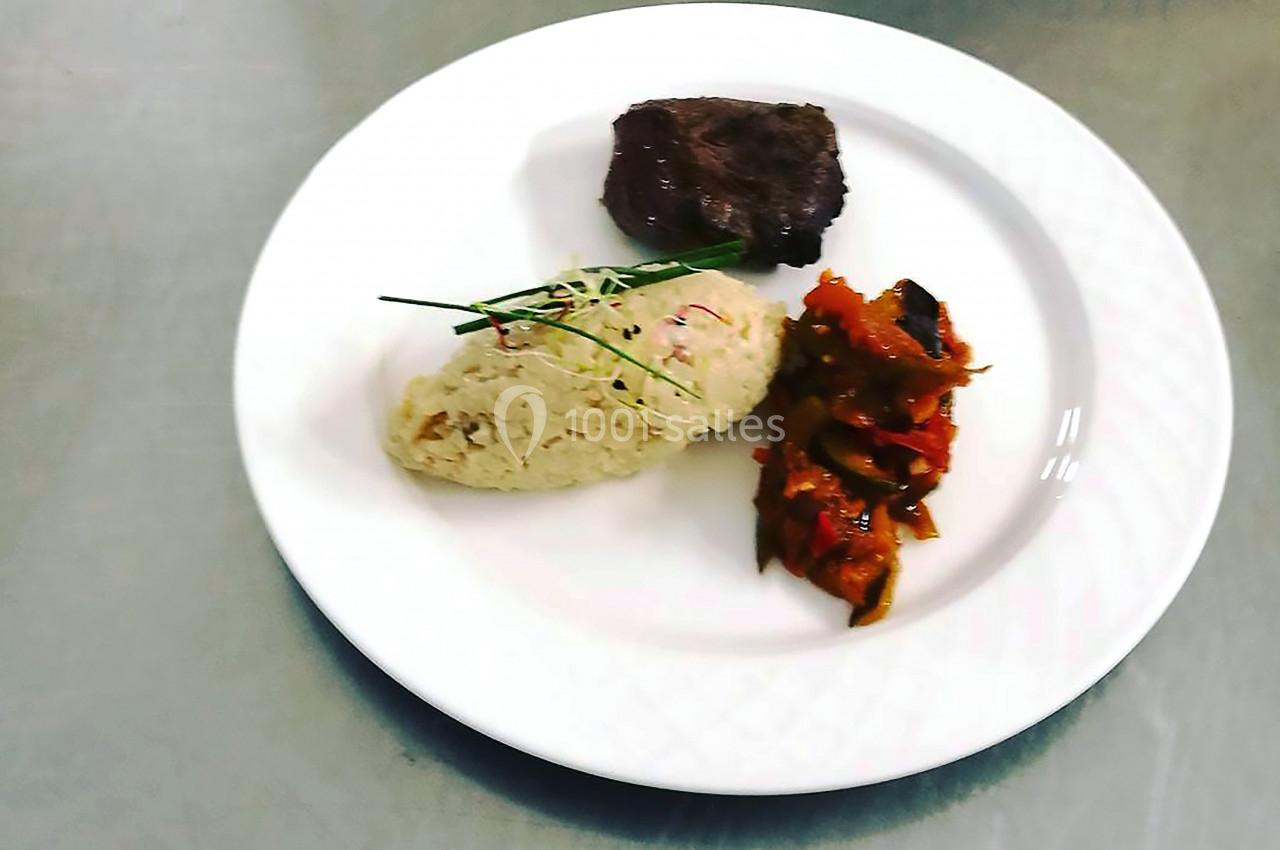 Assiette contenant un morceau de viande, une portion de risotto garni de ciboulette et des légumes mijotés.