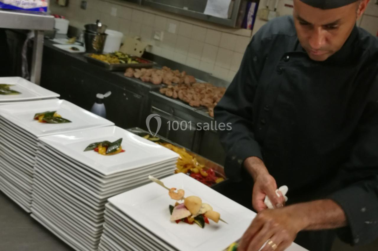 Un chef dispose des assiettes garnies de plats élaborés dans une cuisine professionnelle.