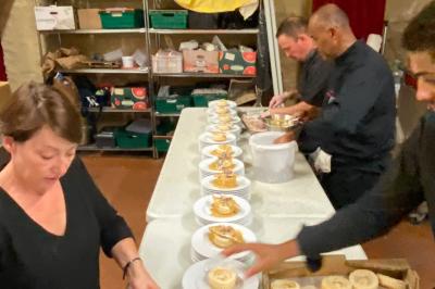Des personnes préparent et disposent des desserts sur des assiettes alignées dans une cuisine professionnelle.