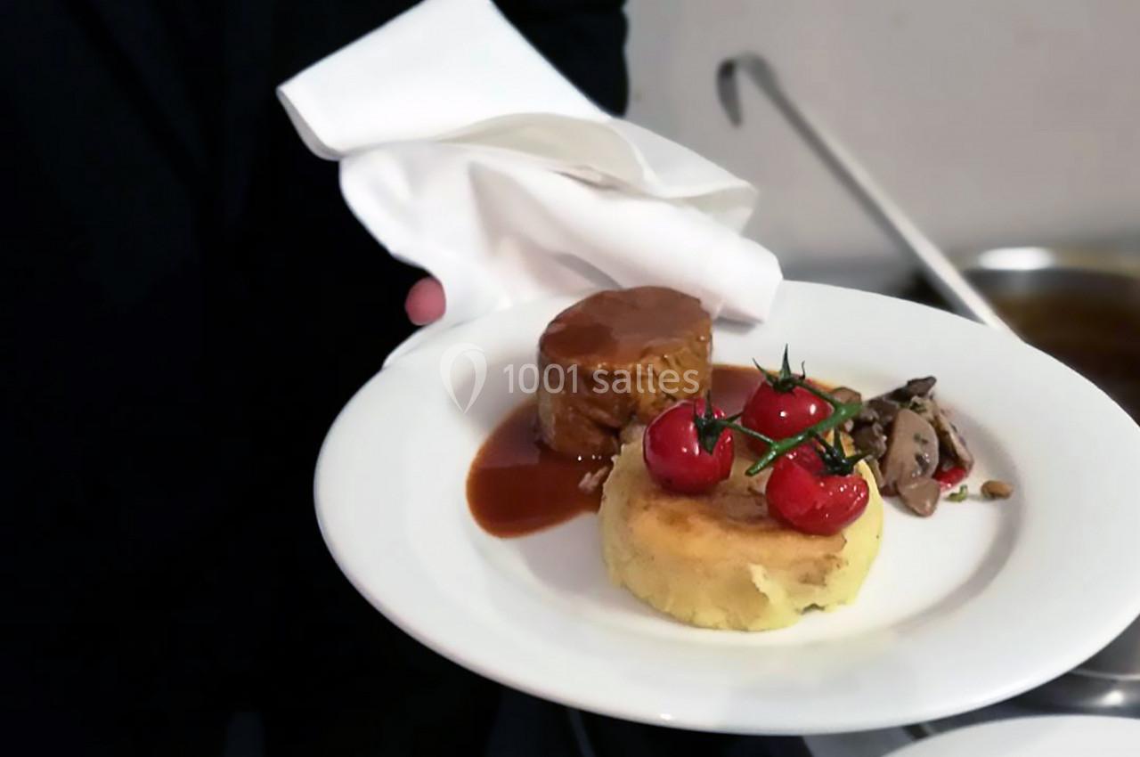 Assiette contenant un morceau de viande en sauce, une purée garnie de tomates cerises et des champignons sautés.