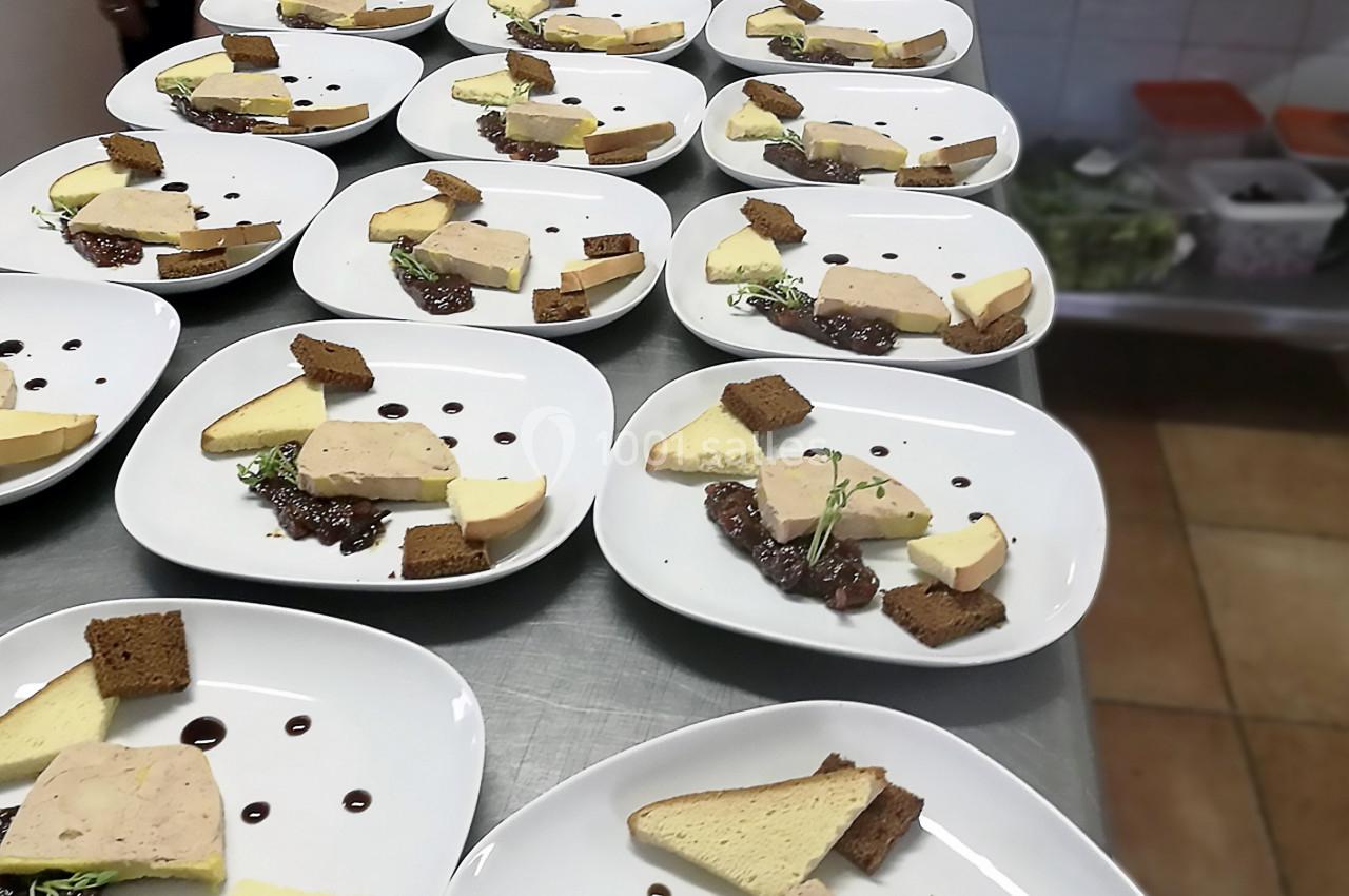Assiettes dressées avec foie gras, pain, confiture et décorations, alignées sur une table dans une cuisine.