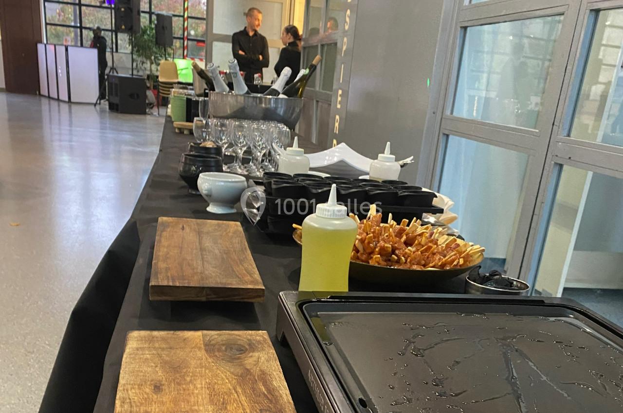 Table de buffet avec planches en bois, verrerie, condiments et brochettes disposées dans un espace intérieur lumineux.