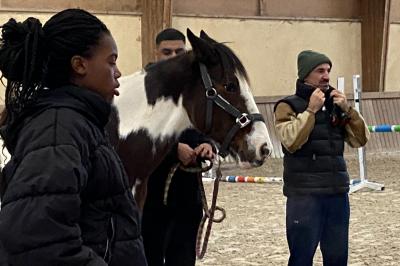 Un homme caresse un cheval blanc attaché par un licol bleu dans un manège en bois.