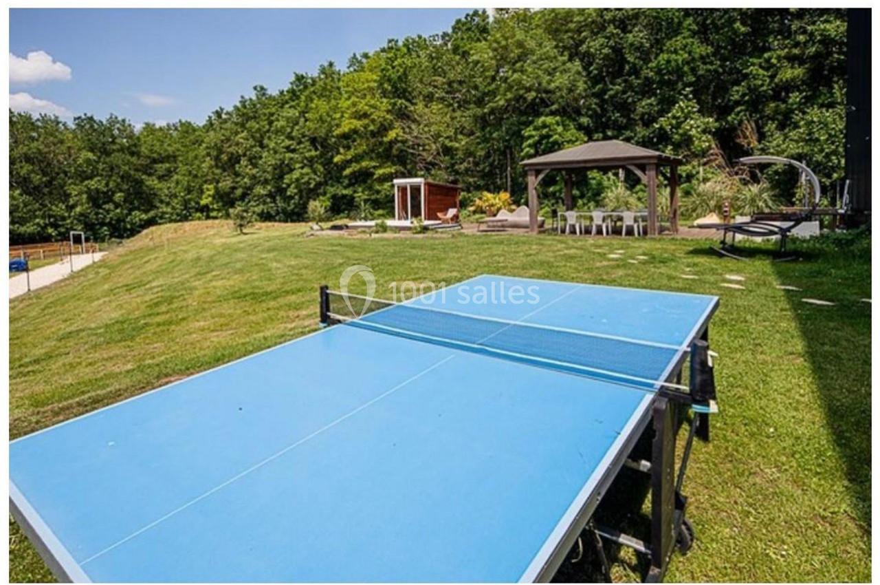 Table de ping-pong bleue installée sur une pelouse, avec un kiosque et des arbres en arrière-plan.