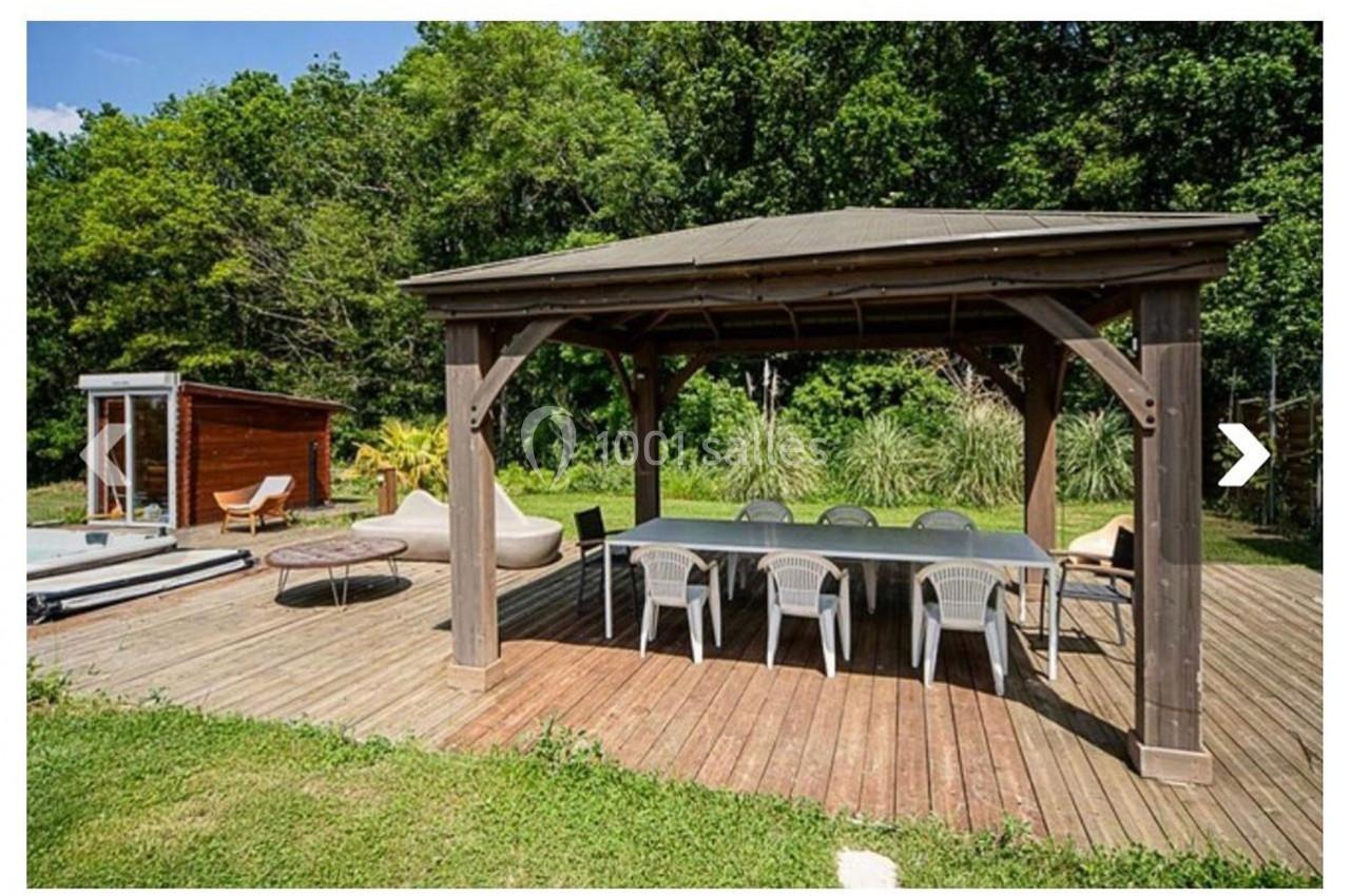 Pergola en bois avec table et chaises sur une terrasse en bois, entourée de verdure et d'un spa extérieur.