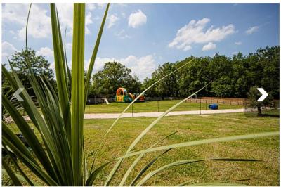 Vue d'un espace extérieur avec pelouse, structures gonflables colorées et arbres en arrière-plan, sous un ciel bleu.