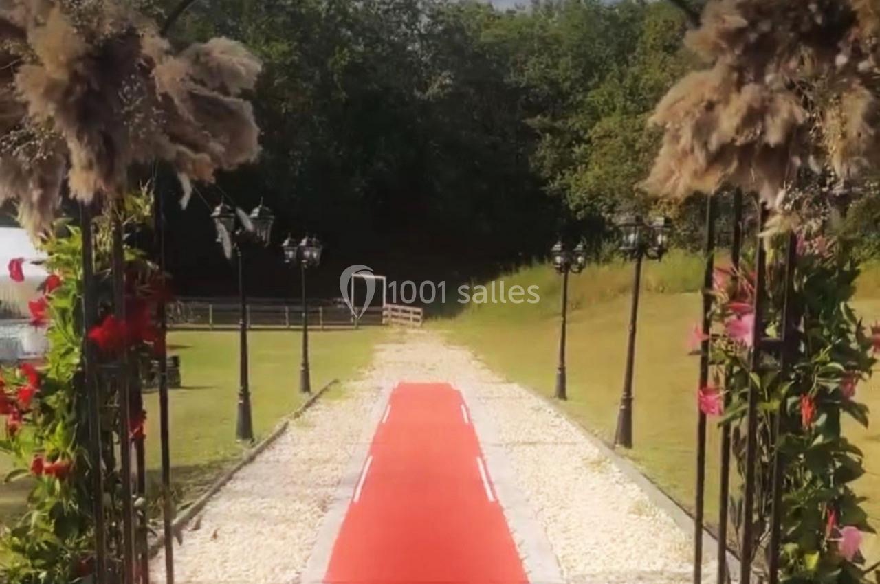 Allée extérieure bordée de lampadaires et décorée de fleurs, avec un tapis rouge menant vers un espace ouvert.