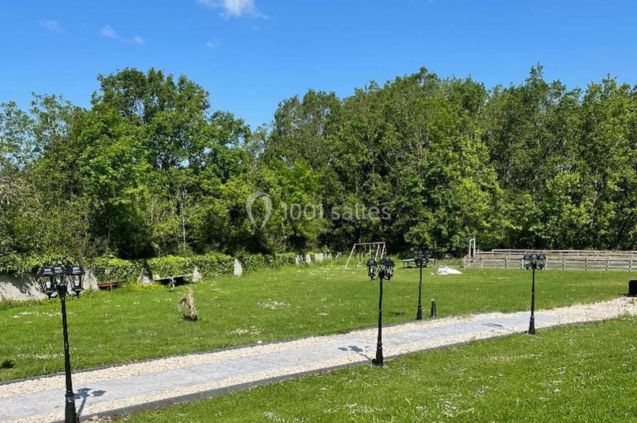 Allée pavée bordée de lampadaires dans un grand jardin verdoyant avec des arbres en arrière-plan.