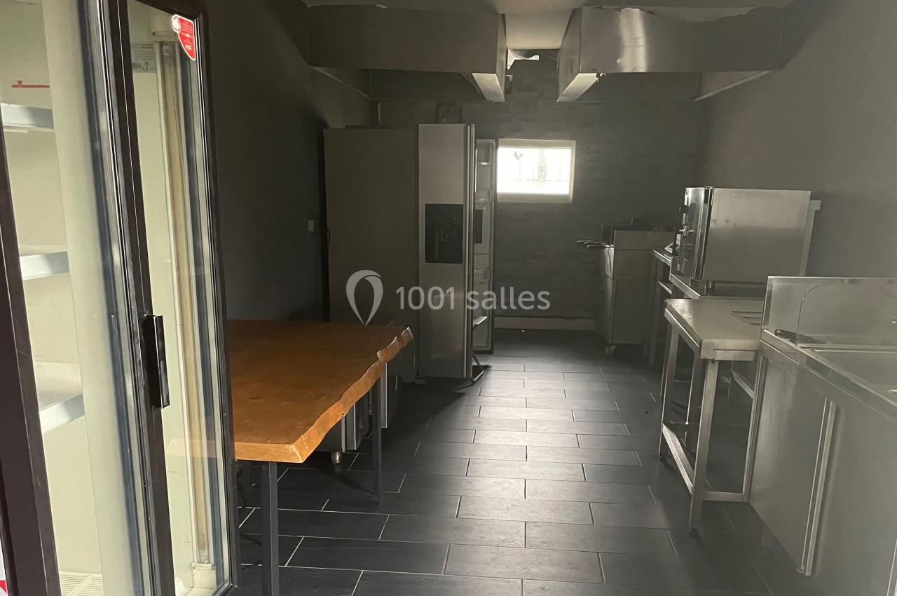 Cuisine professionnelle vide avec équipements en acier inoxydable, réfrigérateur Coca-Cola et plan de travail en bois.