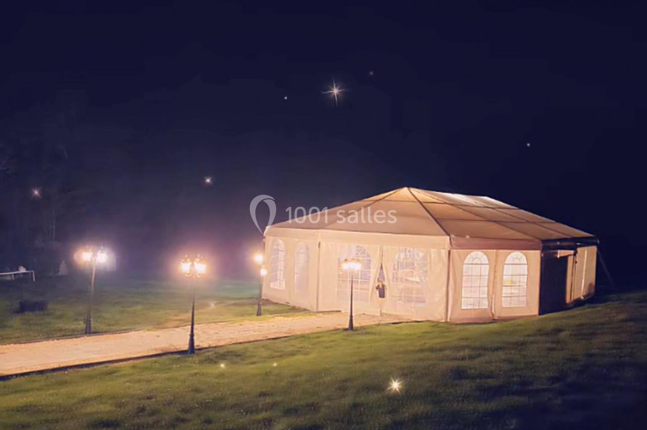 Tente éclairée installée sur une pelouse la nuit, entourée de lampadaires et d'un chemin pavé.