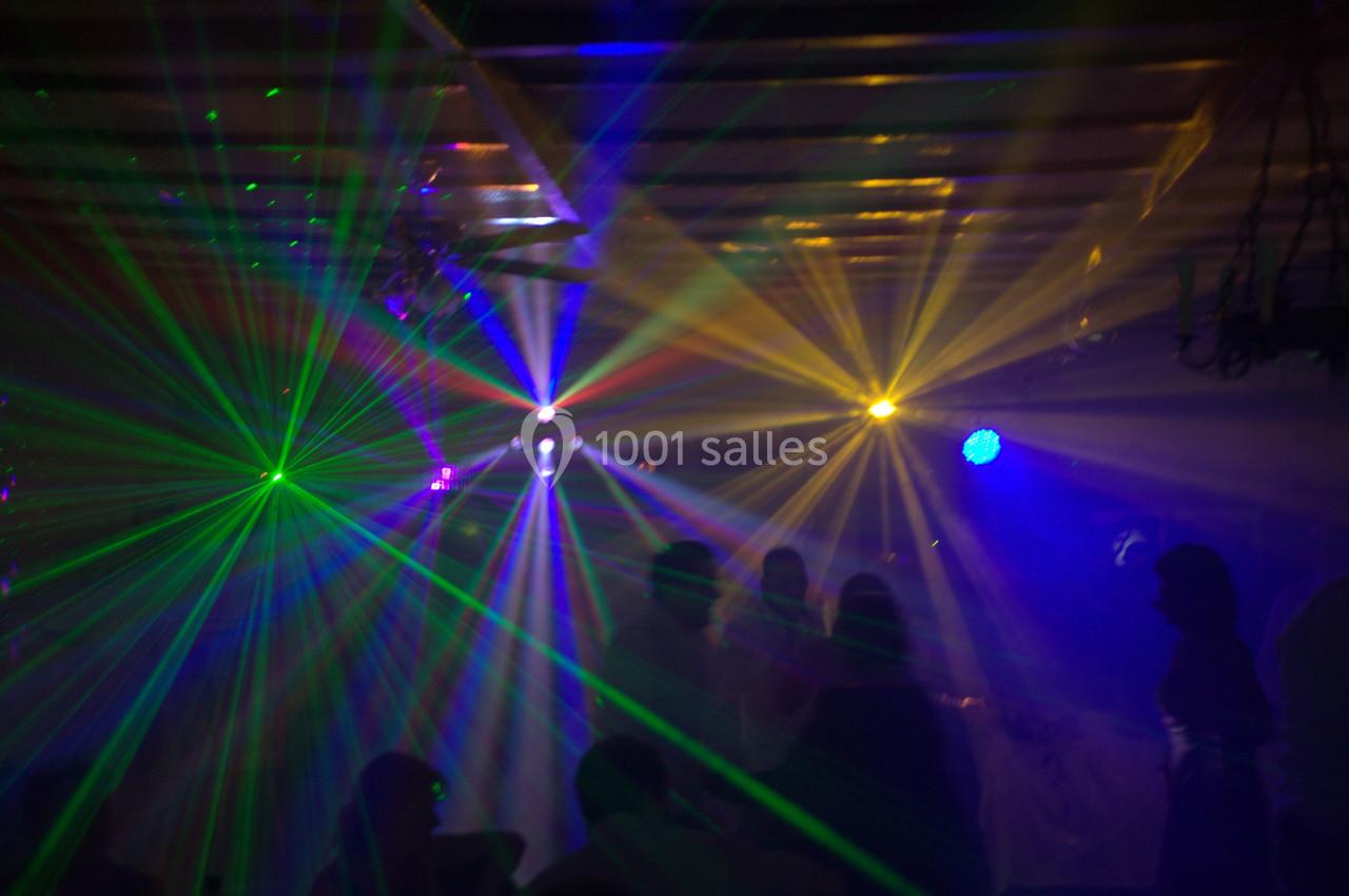 Des faisceaux lumineux colorés traversent une salle sombre remplie de silhouettes de personnes.