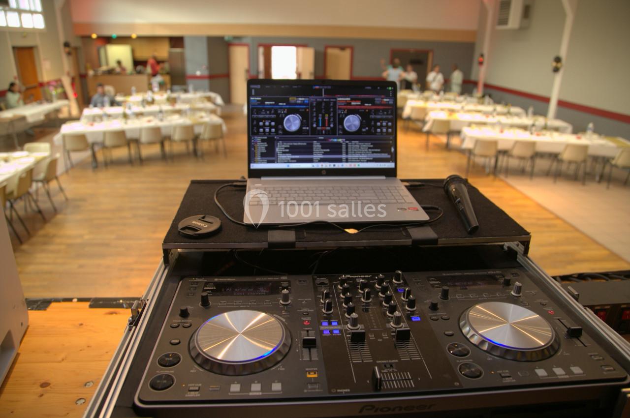 Poste de DJ avec platines et ordinateur portable dans une salle de réception préparée pour un événement.