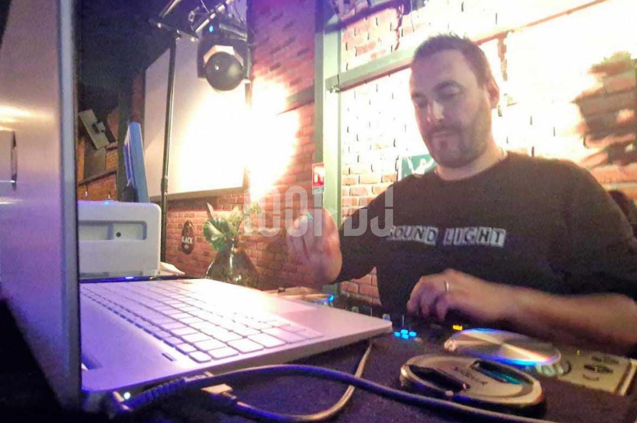 Un DJ mixe de la musique sur une console dans un bar à l'ambiance tamisée avec des lumières chaudes.