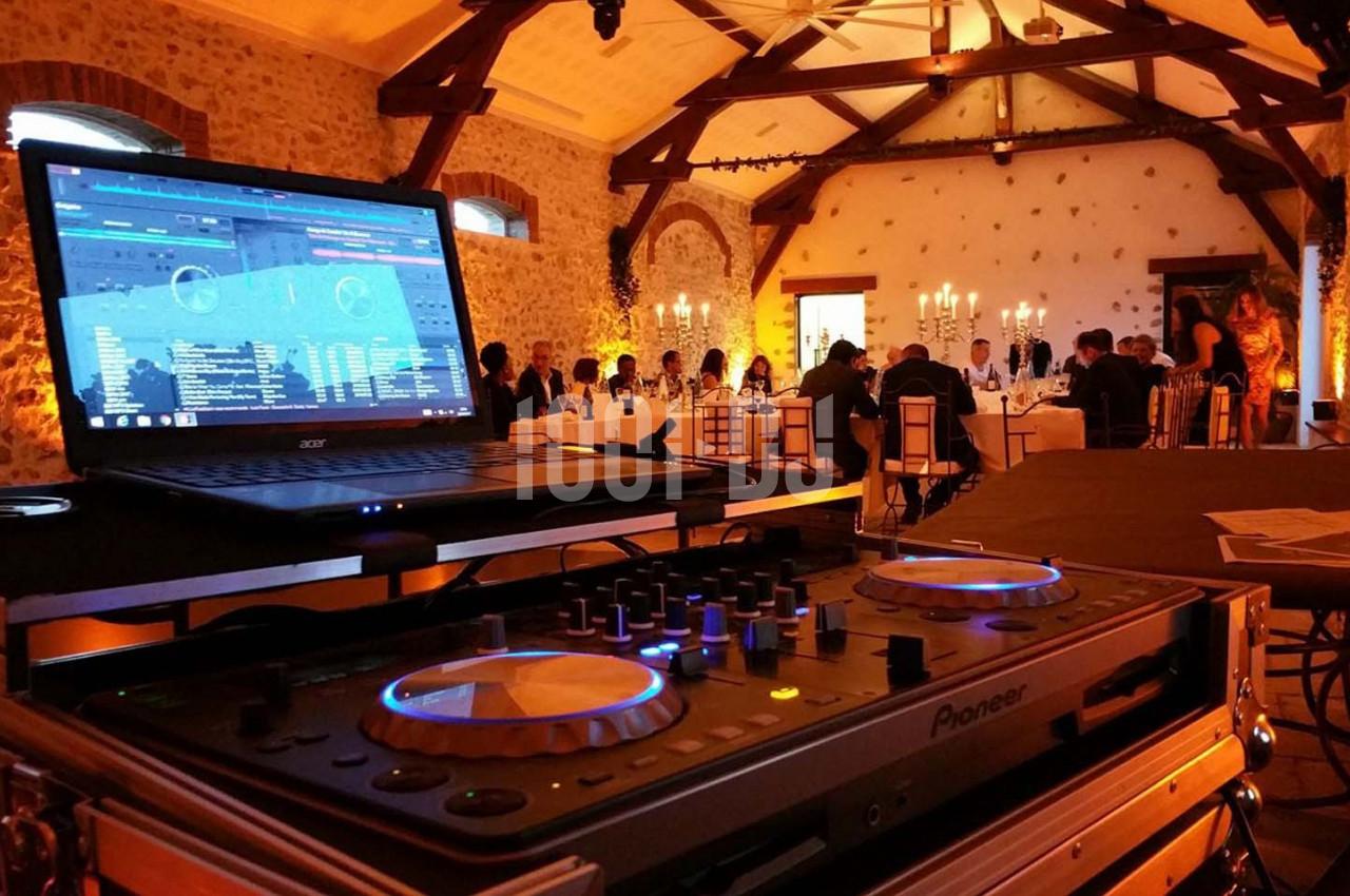 Console de DJ en gros plan dans une salle de réception éclairée, avec des invités attablés en arrière-plan.