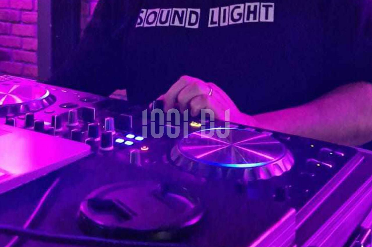 Personne ajustant les commandes d'une table de mixage DJ sous un éclairage violet.