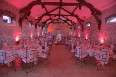 Salle de réception en pierre avec poutres apparentes, tables dressées et éclairage rose tamisé.