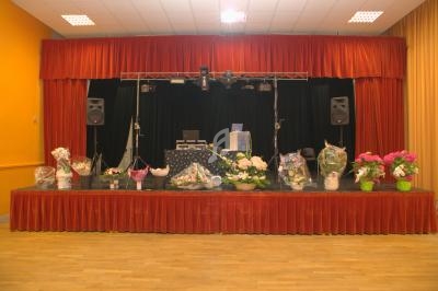 Scène décorée avec des bouquets de fleurs, des équipements audio et un rideau rouge dans une salle.