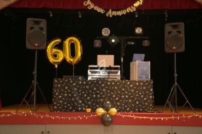 Table de DJ décorée avec des ballons dorés en forme de ’60’, éclairages et enceinte sur une scène festive.