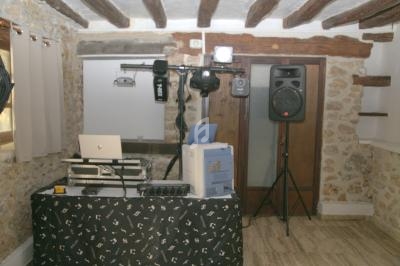 Table de DJ équipée d'un ordinateur portable, d'enceintes et d'éclairages dans une pièce aux murs en pierre apparente.