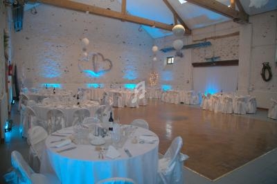 Salle de réception décorée avec des tables rondes dressées, éclairage bleu et murs en pierre apparente.