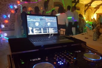Ordinateur portable avec logiciel de mixage sur une table de DJ, devant une piste de danse éclairée par des lumières…