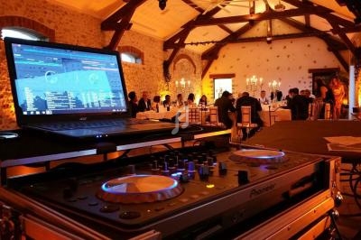 Console de DJ en gros plan dans une salle de réception éclairée, avec des invités attablés en arrière-plan.