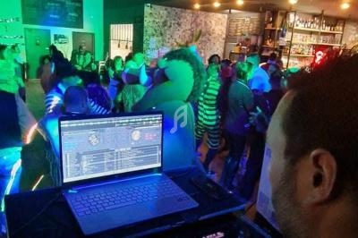 Vue depuis la cabine du DJ sur une piste de danse animée dans un bar avec des lumières colorées.