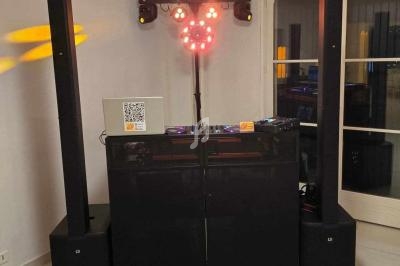 Équipement de DJ avec enceintes, table de mixage et éclairage coloré installé dans une pièce lumineuse.