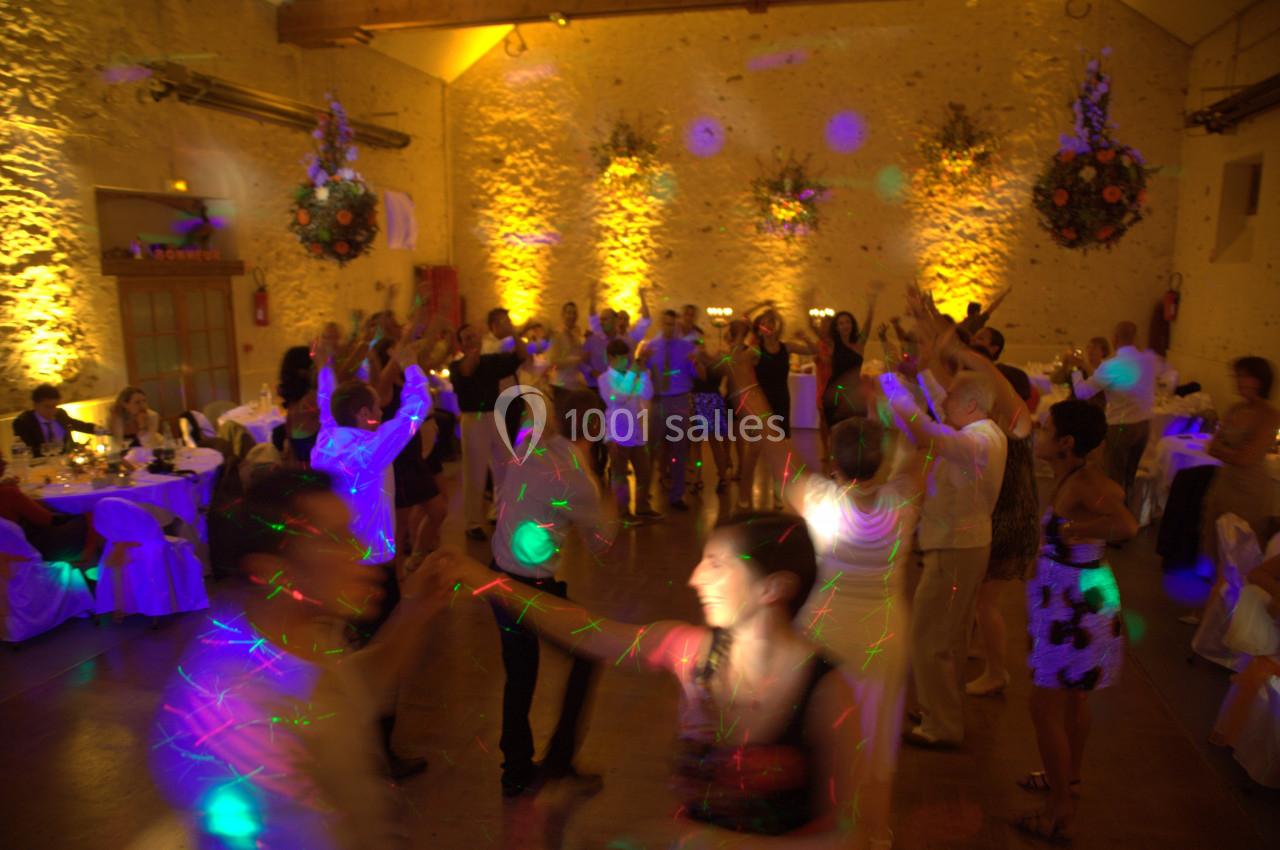 Des personnes dansent dans une salle éclairée par des lumières colorées, avec des murs en pierre et des décorations florales.