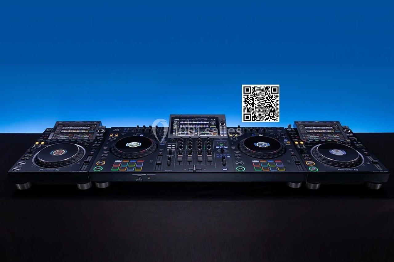 Table de mixage DJ professionnelle avec plusieurs platines, écrans et un QR code visible en arrière-plan.