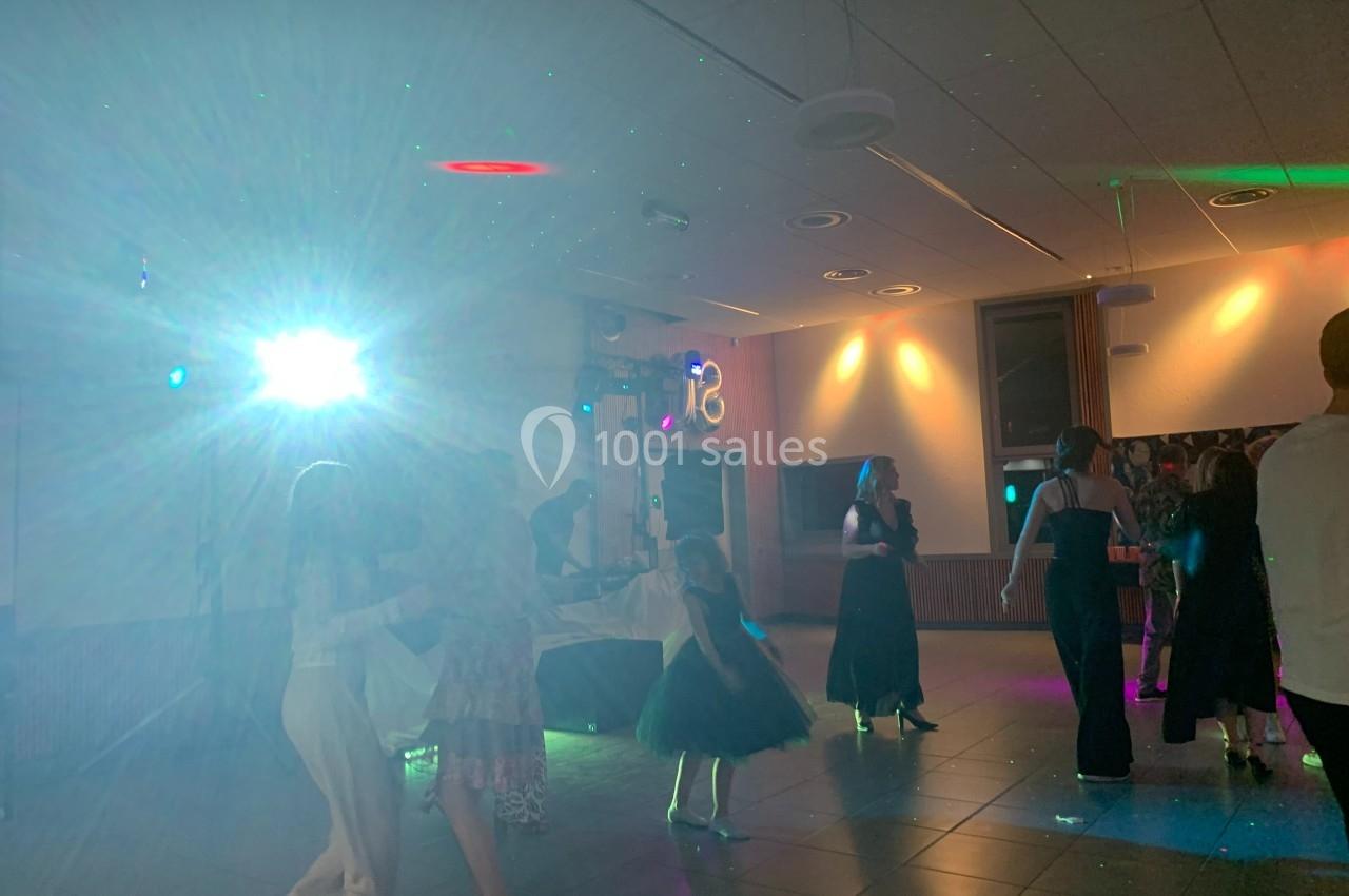 Des personnes dansent dans une salle éclairée par des lumières colorées et un projecteur.