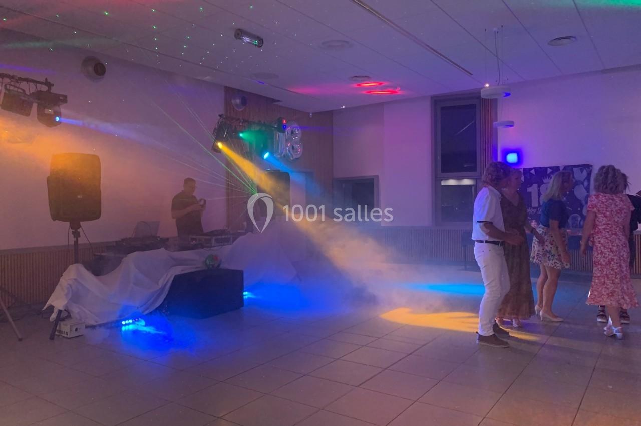 Des personnes dansent dans une salle éclairée par des lumières colorées et des effets de fumée près d'un DJ.