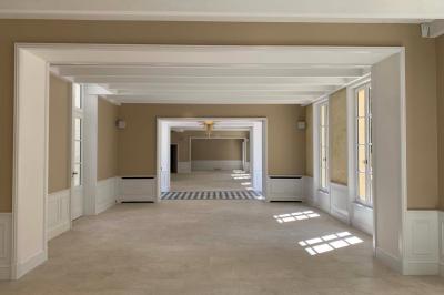 Vue d'un arbre à travers une fenêtre cintrée, encadrée par un intérieur lumineux avec un luminaire suspendu.