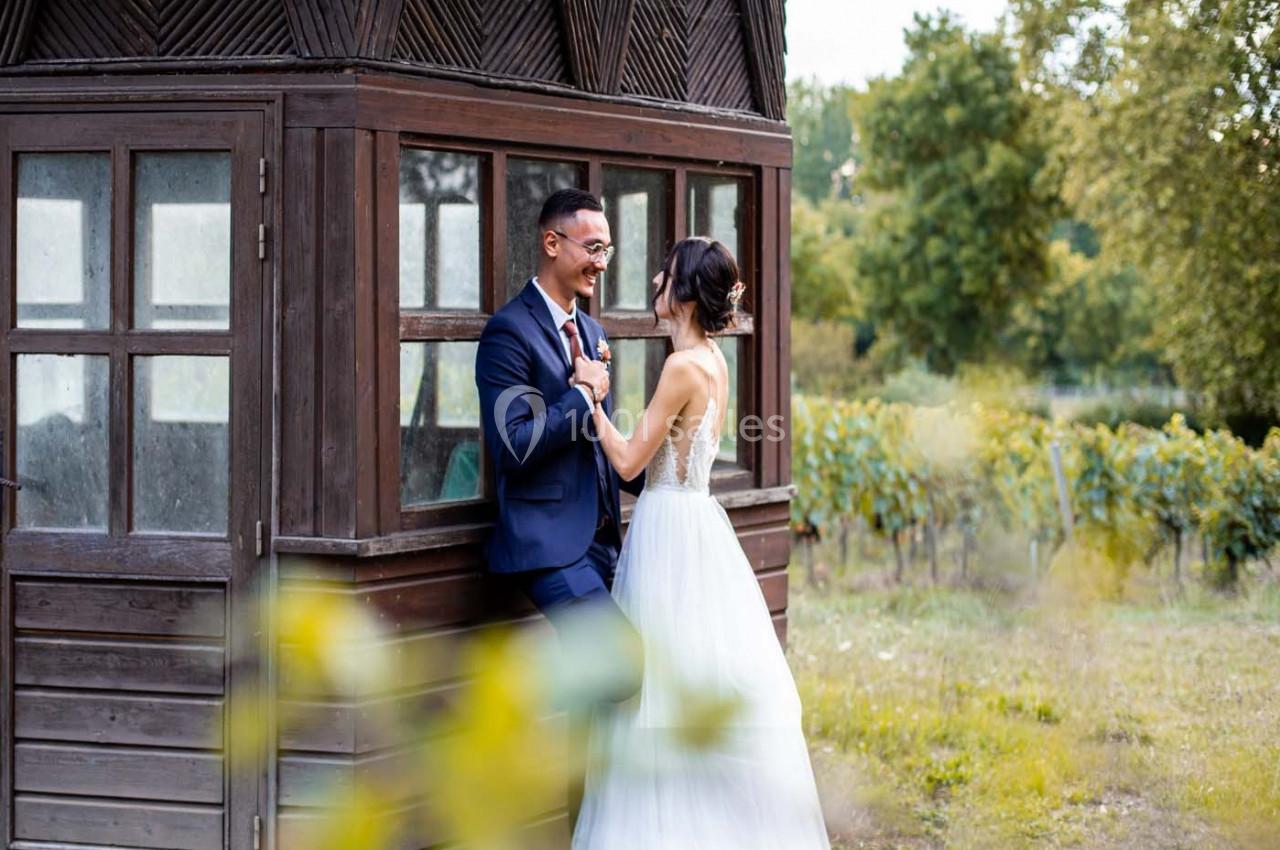 Un couple en tenue de mariage se tient devant une petite cabane en bois, entourée de verdure.