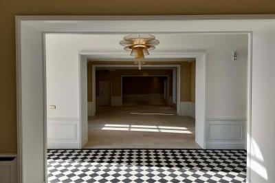 Vue d'un arbre à travers une fenêtre cintrée, encadrée par un intérieur lumineux avec un luminaire suspendu.