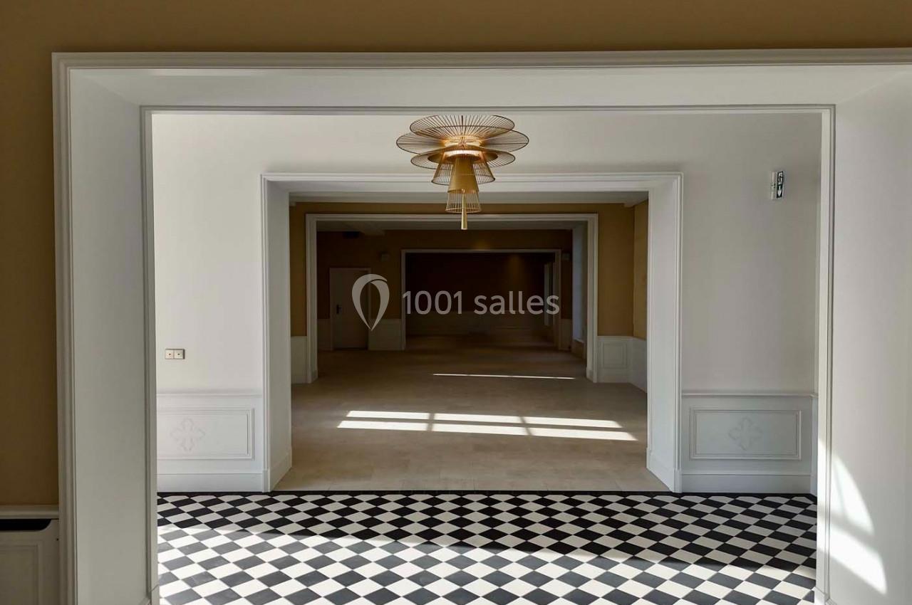 Vue d'une pièce lumineuse avec un sol en damier noir et blanc, des murs clairs et un lustre central doré.