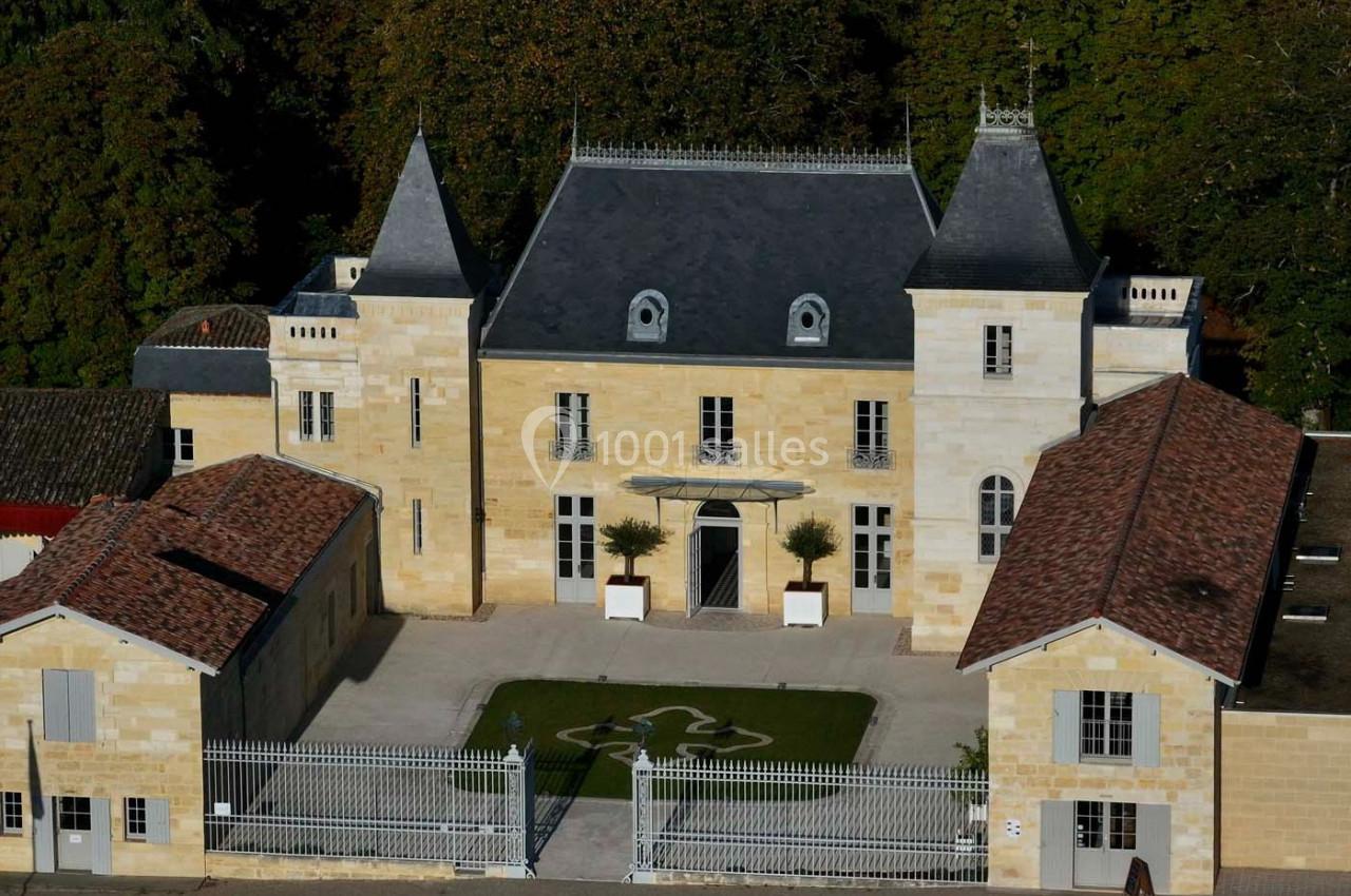 Façade d'un château en pierre avec deux tours, entouré de dépendances et d'une grille en fer forgé.