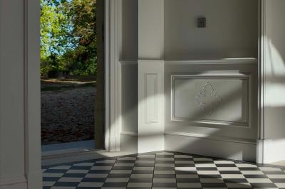 Vue d'un arbre à travers une porte vitrée, encadrée par un intérieur lumineux avec un luminaire suspendu.