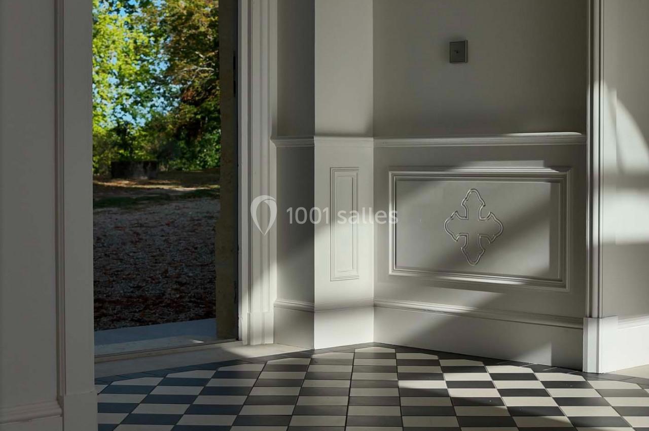 Sol en damier noir et blanc dans une pièce lumineuse avec une porte ouverte sur un jardin arboré.