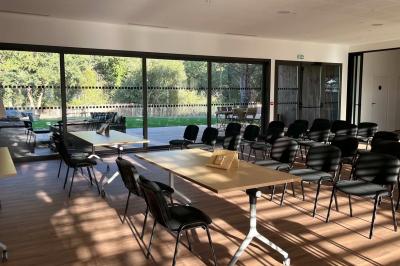 Chambre lumineuse avec lit double, bureau, coin salon, kitchenette et vue sur un jardin à travers une baie vitrée.