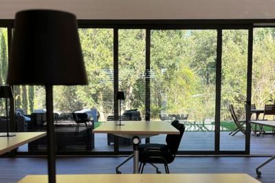 Chambre lumineuse avec lit double, bureau, coin salon, kitchenette et vue sur un jardin à travers une baie vitrée.