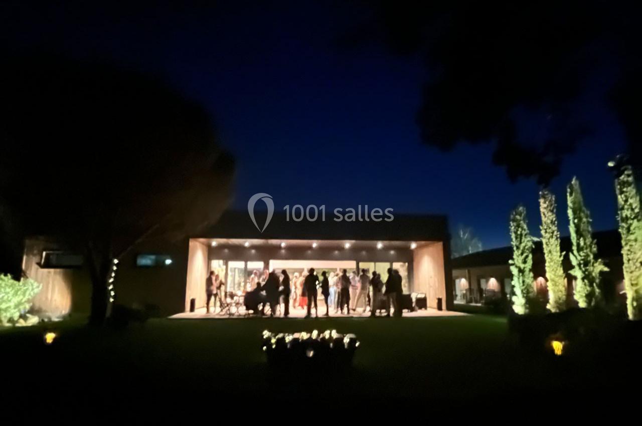 Groupe de personnes rassemblées sur une terrasse éclairée, entourée de végétation, en soirée.