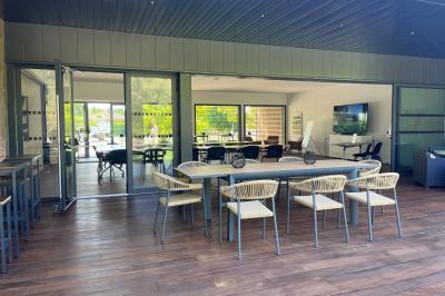 Chambre lumineuse avec lit double, bureau, coin salon, kitchenette et vue sur un jardin à travers une baie vitrée.