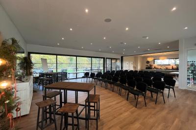 Chambre lumineuse avec lit double, bureau, coin salon, kitchenette et vue sur un jardin à travers une baie vitrée.