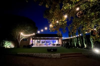 Chambre lumineuse avec lit double, bureau, coin salon, kitchenette et vue sur un jardin à travers une baie vitrée.