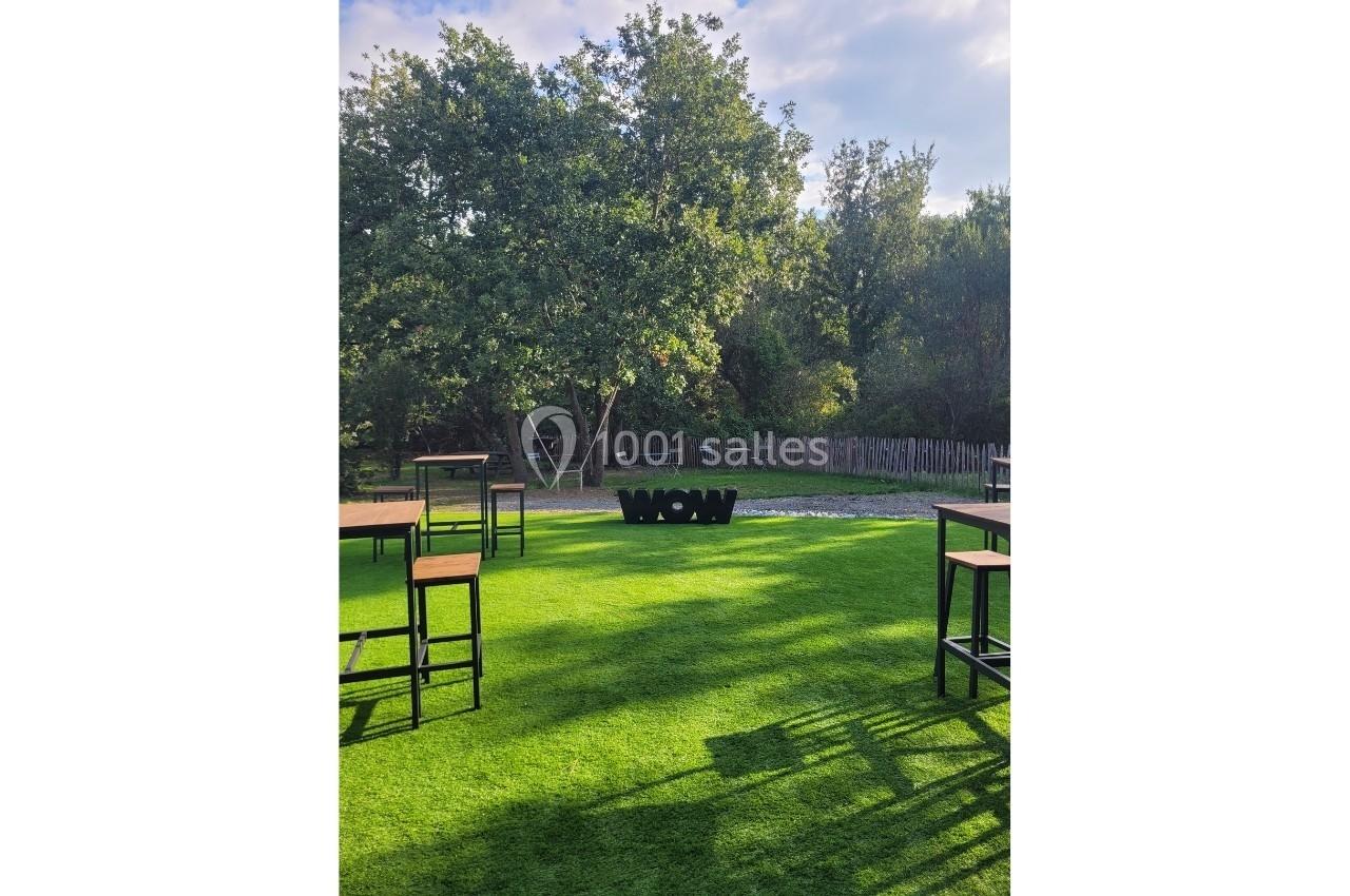 Tables hautes disposées sur une pelouse verte, avec des arbres en arrière-plan et le mot ’WOW’ en lettres noires.