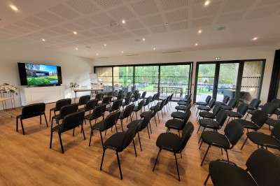Chambre lumineuse avec lit double, bureau, coin salon, kitchenette et vue sur un jardin à travers une baie vitrée.