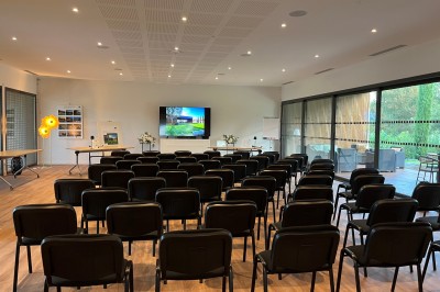 Chambre lumineuse avec lit double, bureau, coin salon, kitchenette et vue sur un jardin à travers une baie vitrée.